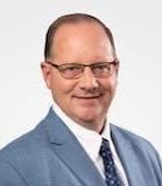 Balding man with dark hair and glasses smiles. He has a gray suit on.